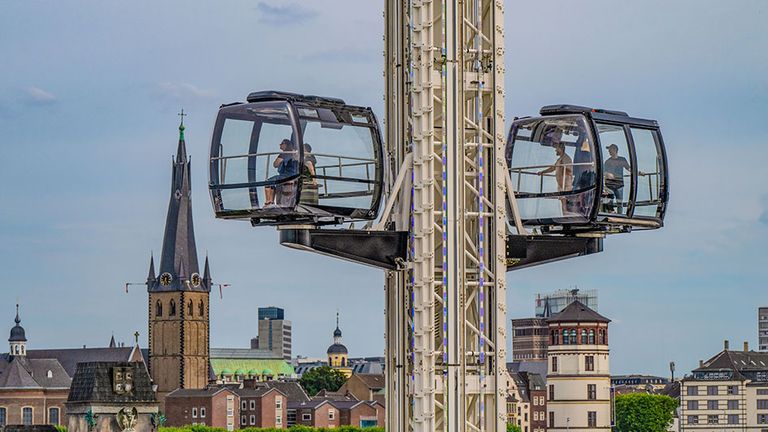 Zwei Gondeln einer Seilbahn über historischer Stadt mit Kirchturm im Hintergrund.