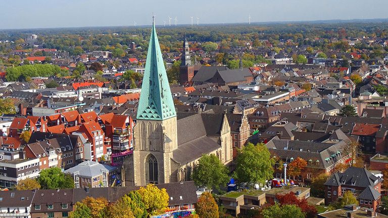 Aussicht auf historische Stadt mit markanter Kirche und grünem Turm, umgeben von Dächern und Bäumen.